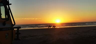 Un coucher de soleil sur la plage avec des chevaux au loin.