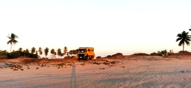 Un camion jaune sur une plage au coucher du soleil.