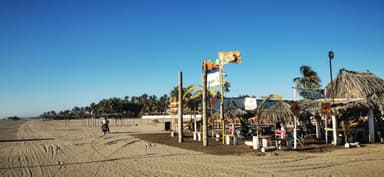 Une plage avec des palapas et des drapeaux sous un ciel bleu.