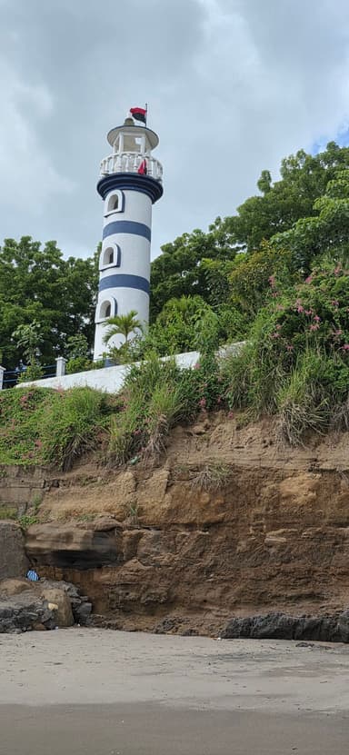 Un phare rayé sur une plage avec des nuages en arrière-plan.