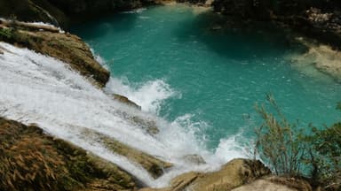 Une cascade d'eau claire se déversant dans une piscine naturelle turquoise.