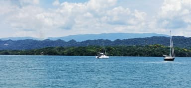 Deux voiliers naviguant sur un lac entouré de montagnes sous un ciel nuageux.