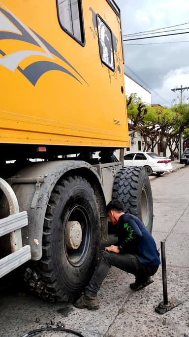 A person working on a large yellow vehicle's tire on a street.