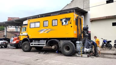 A yellow overland truck parked on a street with a mechanic working nearby.
