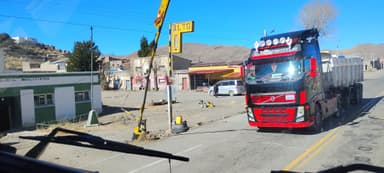 A red truck passing by a roadside sign in a rural area.