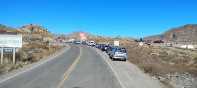 A winding road with parked cars and rocky hills under a clear blue sky.