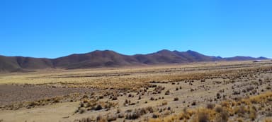 A vast landscape of rolling hills and sparse vegetation under a clear blue sky.