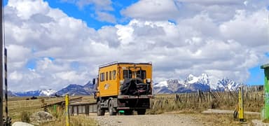 Un camion orange sur une route avec des montagnes en arrière-plan sous un ciel nuageux.