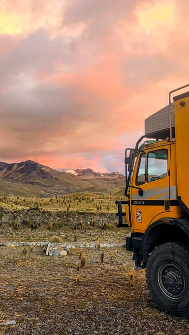 Un camion orange devant un paysage montagneux au coucher du soleil.