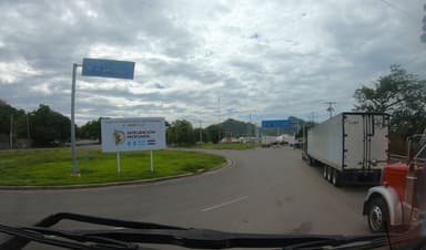 Un rond-point avec des camions et des panneaux de signalisation sous un ciel nuageux.