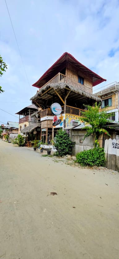 Une maison en bois sur une rue de sable, avec des plantes vertes autour.