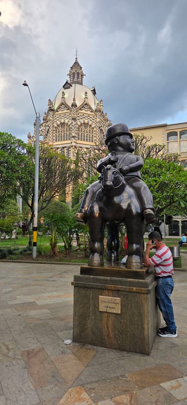 Une statue en bronze d'un homme sur un cheval dans un parc avec un bâtiment en arrière-plan.