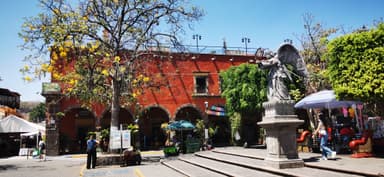 Une place animée avec un arbre et une statue d'ange sous un ciel bleu.