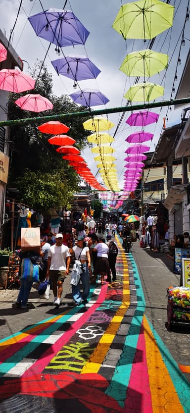 Une rue colorée avec des parapluies suspendus et des gens marchant.