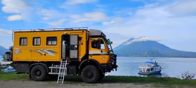 Un camion jaune près d'un lac avec des montagnes en arrière-plan.