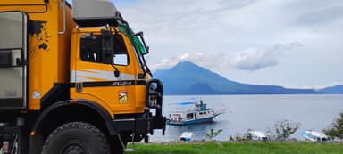 Un camion jaune près d'un lac avec des montagnes en arrière-plan.