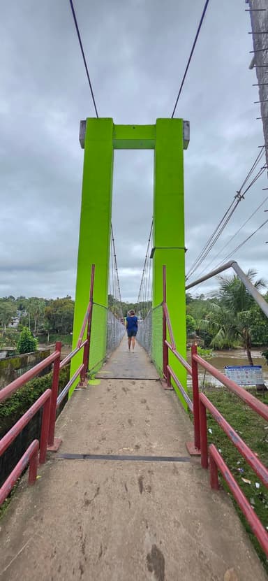 Un pont suspendu vert avec un homme marchant dessus sous un ciel nuageux.