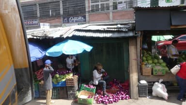 Un marché animé avec des fruits et des vendeurs sous des parasols.
