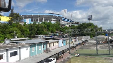Un paysage urbain avec un stade et des maisons colorées sous un ciel nuageux.