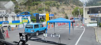 Un point de contrôle routier avec des panneaux et des véhicules sous un ciel nuageux.