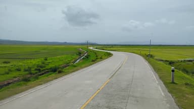 Une route sinueuse à travers des champs verdoyants sous un ciel nuageux.