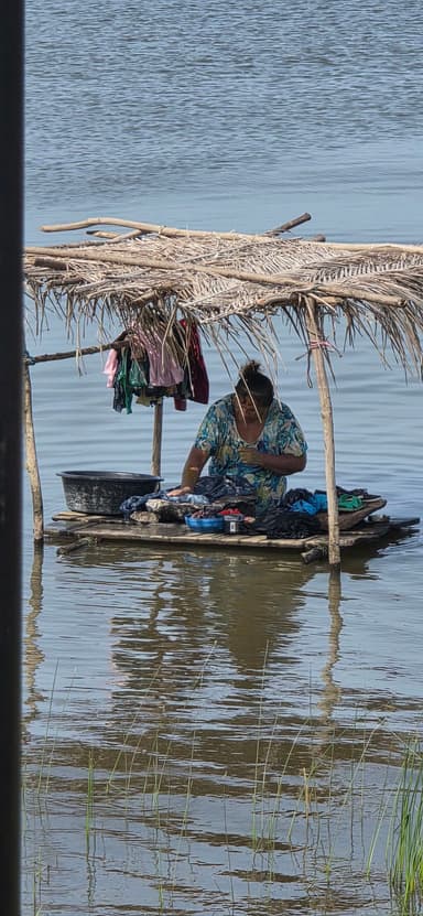 Une femme lave des vêtements sur une plateforme flottante dans l'eau.