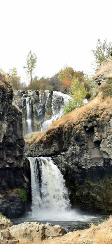 Une cascade entourée de rochers et d'arbres en automne.