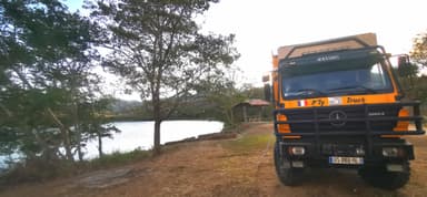 Un camion orange près d'un lac entouré d'arbres.