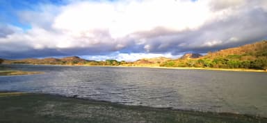 Un paysage naturel avec un lac et des collines sous un ciel nuageux.