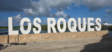 Un grand panneau avec le nom de Los Roques au bord de l'eau.