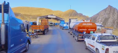 A busy road with trucks and vehicles under a clear blue sky in a mountainous area.