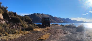 A truck parked by a lake with mountains in the background under a clear blue sky.
