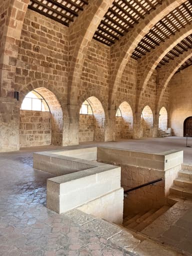 Une grande salle avec des arches en pierre et des fenêtres lumineuses.
