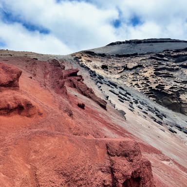 A colorful volcanic landscape with red and black rock formations under a cloudy sky.