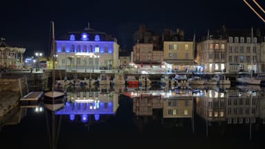 A nighttime view of a harbor with illuminated buildings reflecting in the water.