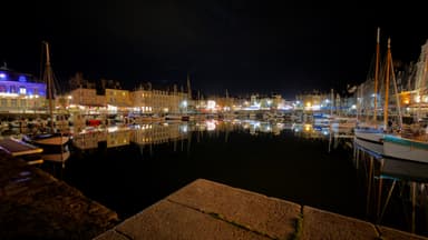 A nighttime view of a harbor with reflections of buildings and boats in the water.