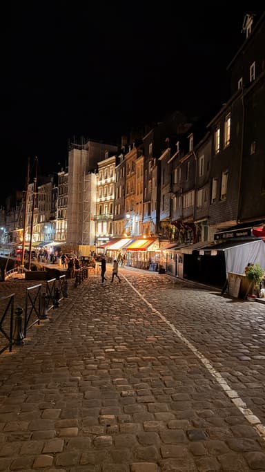 A cobblestone street at night with lit buildings and people walking.