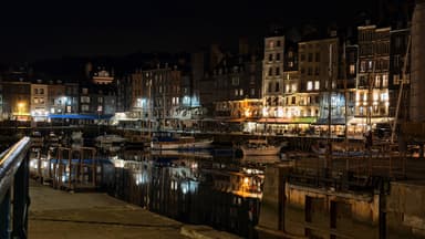 A nighttime view of a harbor with illuminated buildings reflecting on the water.