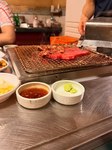 Grilled meat on a barbecue grill with dipping sauces.