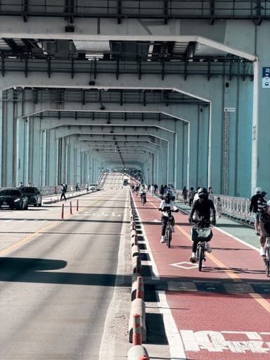 A view of a bike lane under a bridge with cyclists and vehicles.