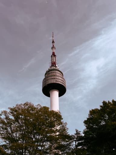 A tall tower surrounded by trees under a cloudy sky.