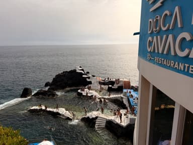 A rocky coastline with people swimming and lounging near a restaurant in Madeira.
