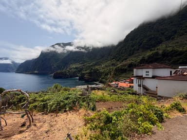 A scenic view of cliffs and ocean with a house and terraced fields in Madeira.