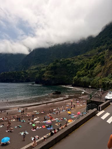 A beach scene in Madeira with people sunbathing and mountains in the background.