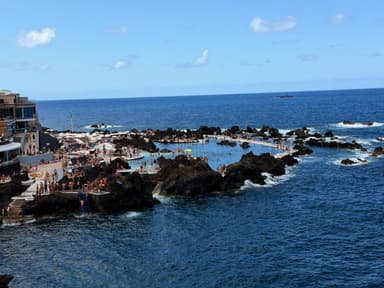A rocky coastline with a pool area and people enjoying the sun.