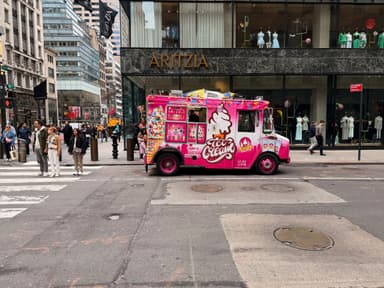 A colorful ice cream truck parked on a busy street with pedestrians nearby.