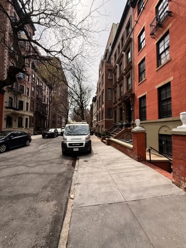 A quiet street in New York with brownstone buildings and a parked van.