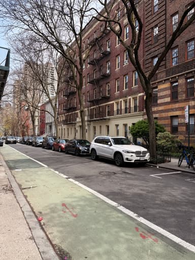A quiet street in New York with parked cars and brownstone buildings.