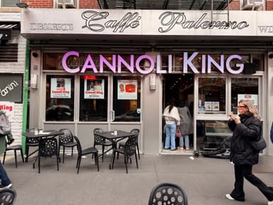 A storefront of Cannoli King with people entering and tables outside.