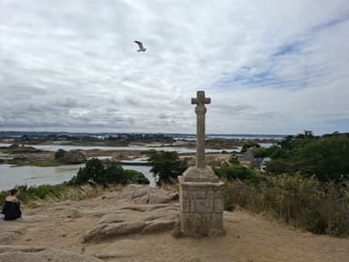 A stone cross overlooking a coastal landscape with a cloudy sky.